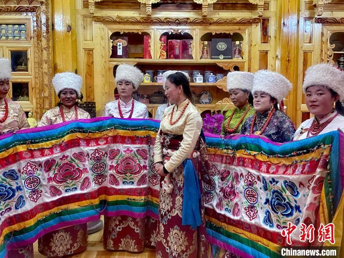 圖為女性展示村民自發(fā)繡制的“百米五彩哈達(dá)”?！±钣穹?攝